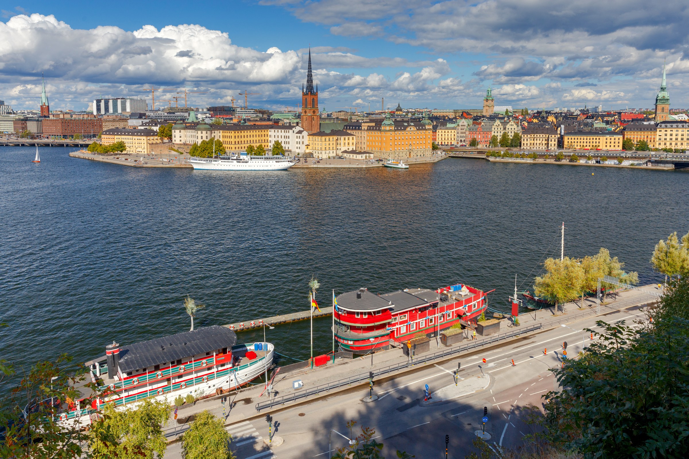 Old town buildings and a church spire across wide water, with red and white boats moored on the quay