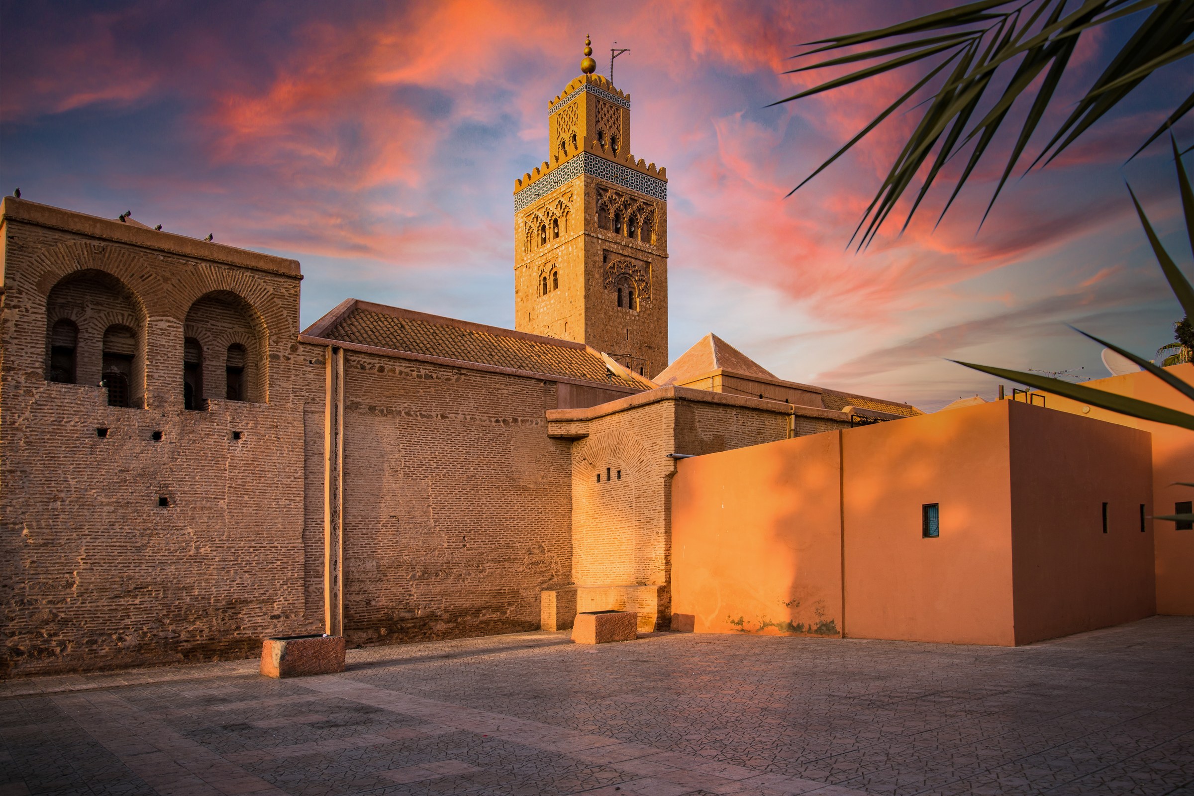 Koutoubia Mosque minaret in Marrakech at sunset with palm trees and a warm orange sky