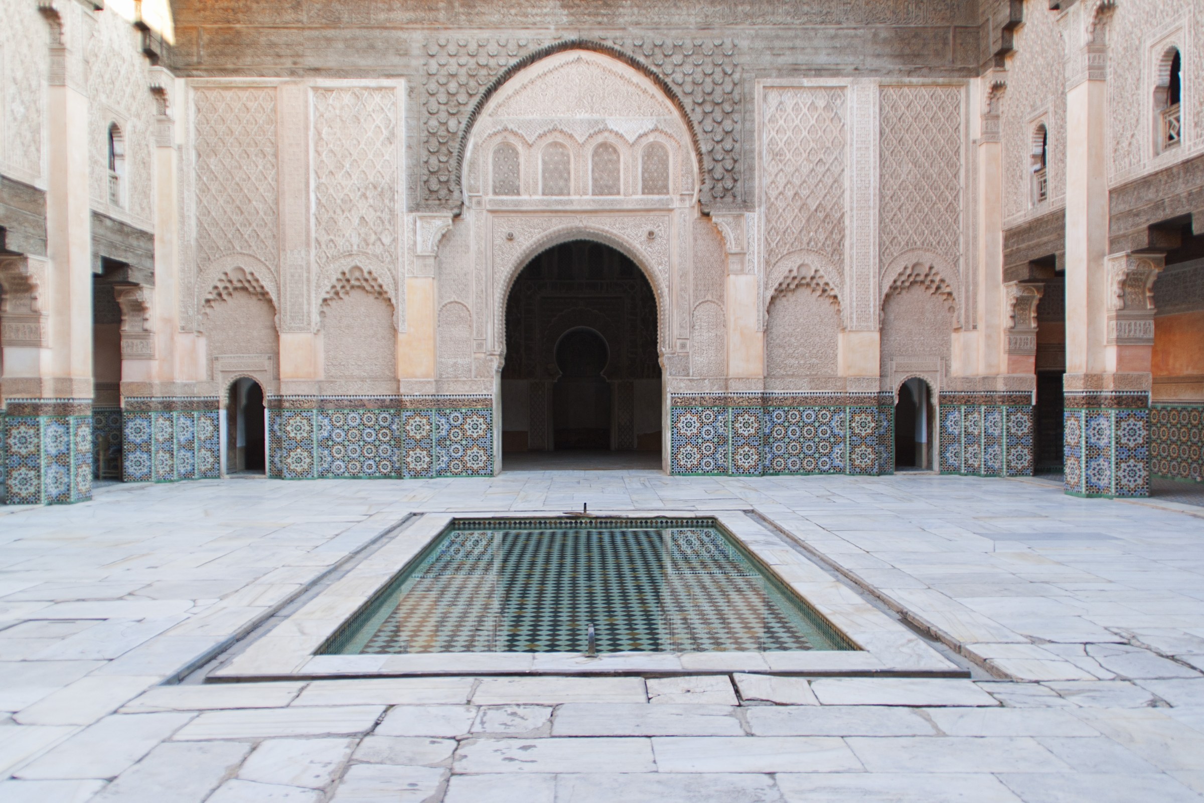 Ornate Moroccan courtyard with carved stucco arches, tiled walls and a rectangular pool