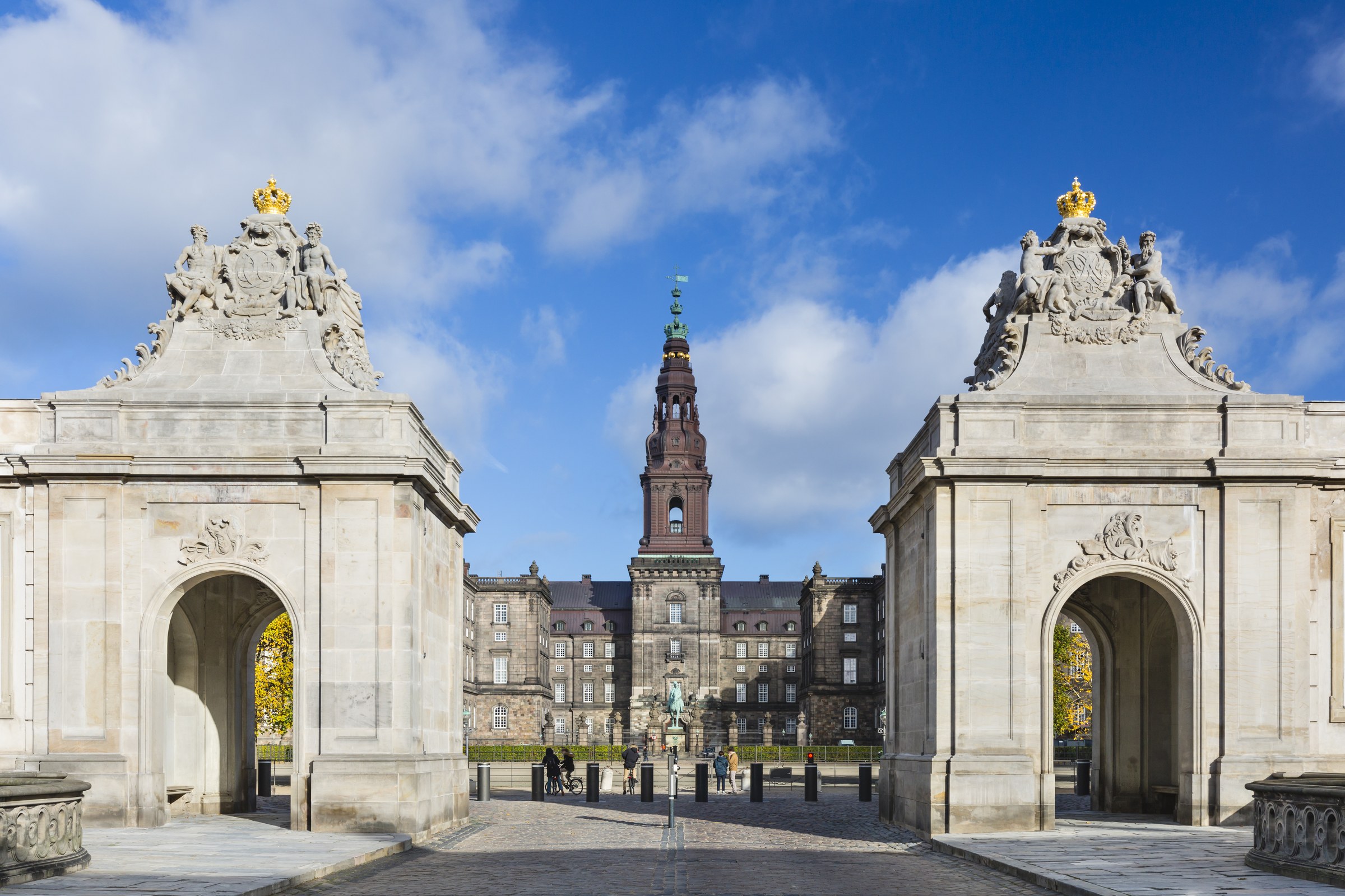 A tall palace tower framed between two stone gate pavilions crowned with gilded crowns, blue sky