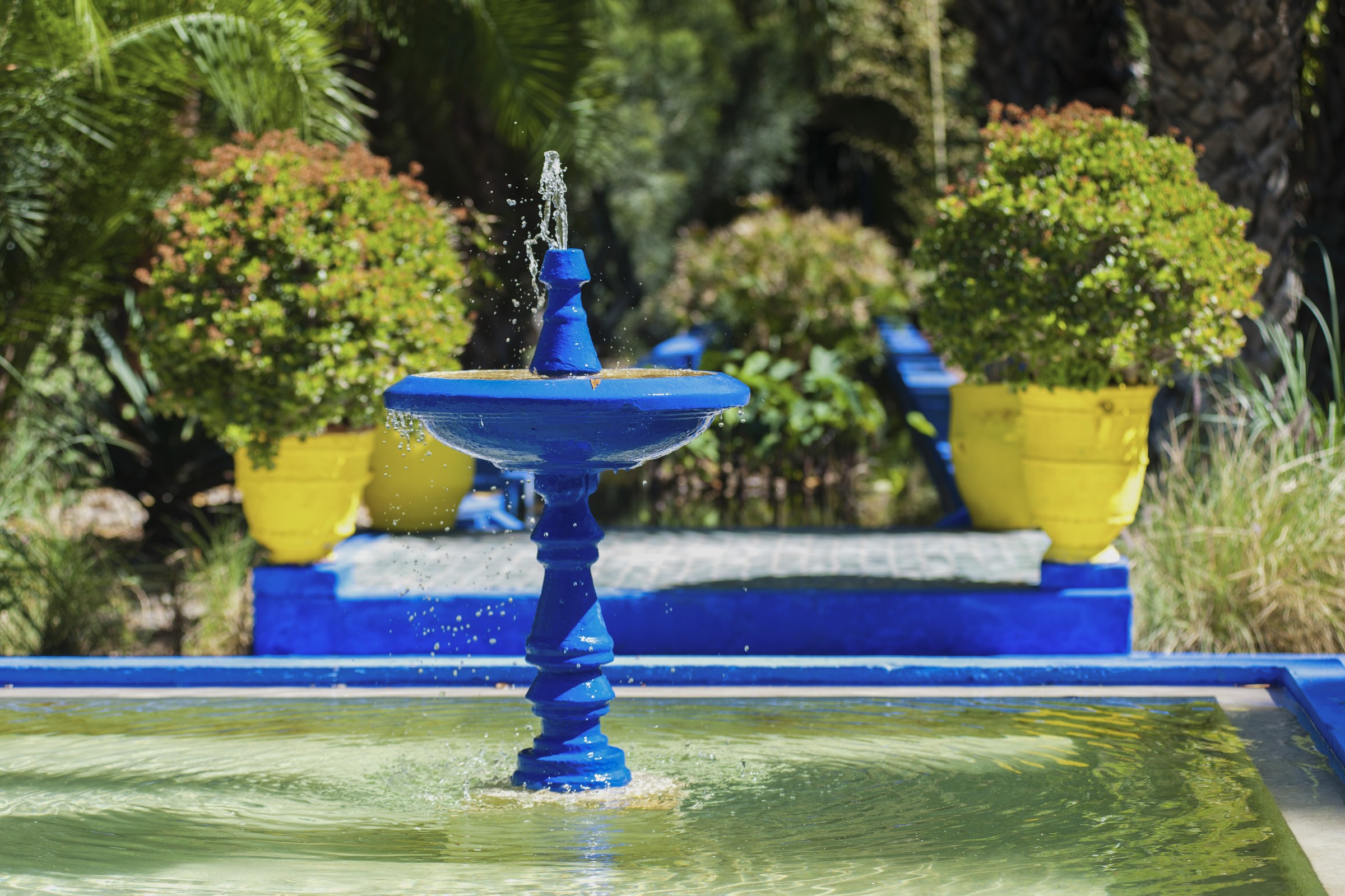 Bright blue fountain surrounded by yellow pots and green plants at Majorelle Garden