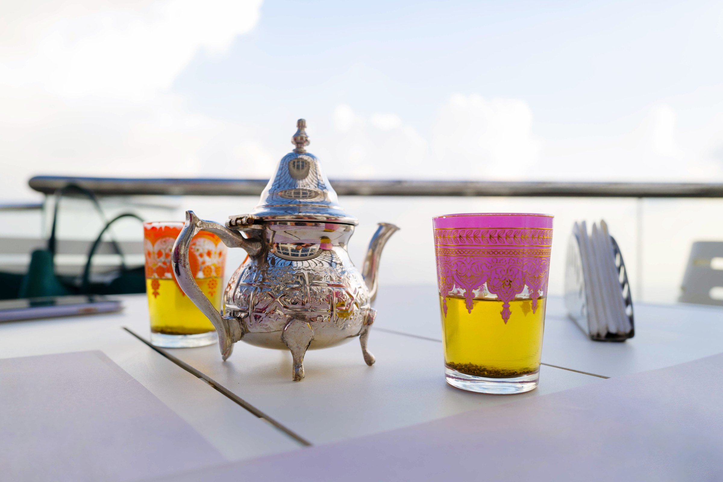 Silver Moroccan teapot and colourful tea glasses on a sunny terrace table
